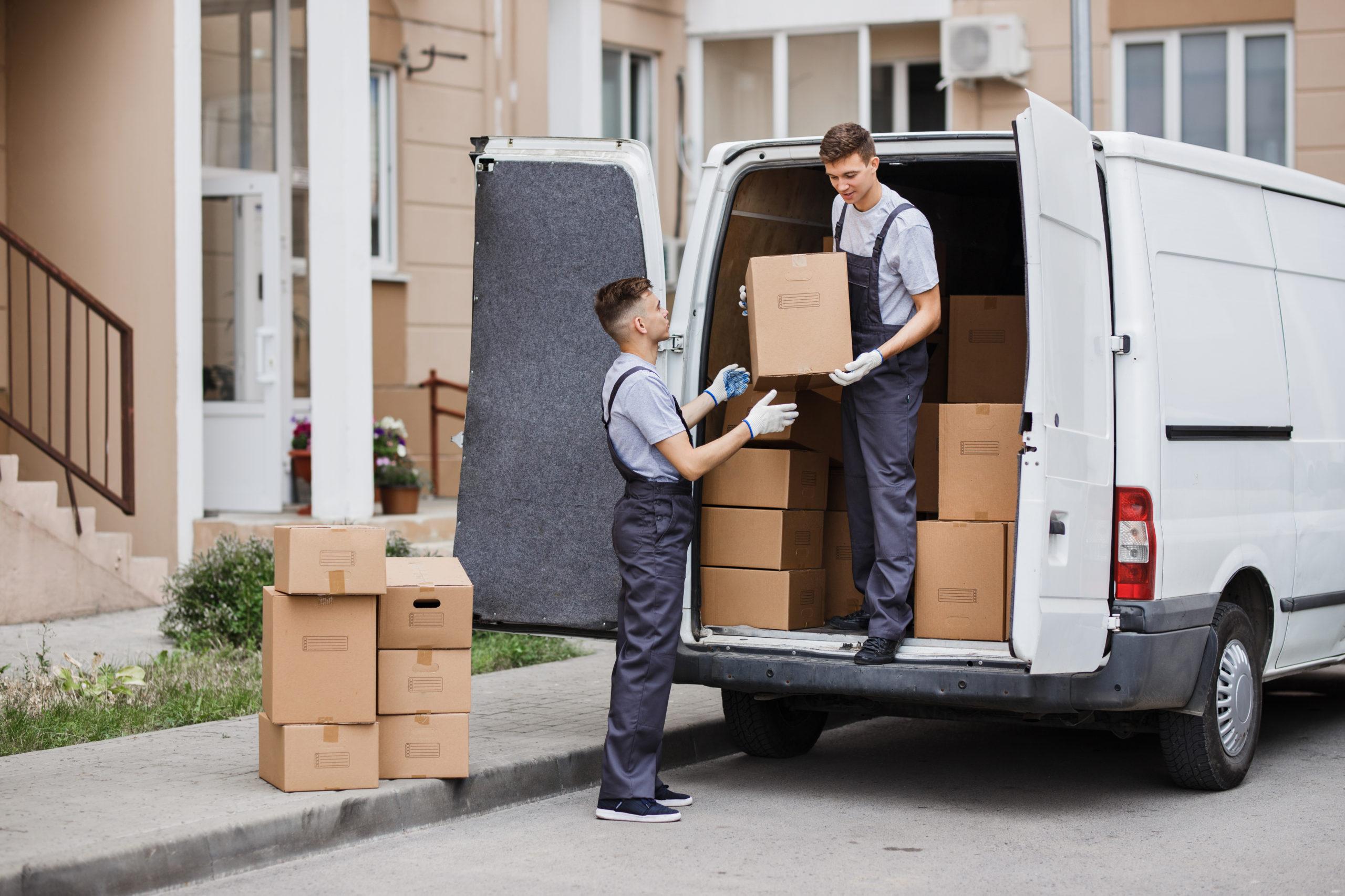 Two young handsome movers wearing uniforms are unloading the van full of boxes.